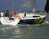Voile rapide, le voilier "Clifden Pour la Vie" navigue sur une mer agitée. Deux personnes sont à bord, profitant du soleil.
