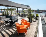 Solig rooftop bar i Göteborg med orangea fåtöljer och utsikt över hamnen.