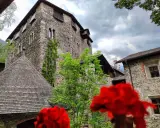 Il castello di Campo Tures, con le sue mura in pietra e il tetto a scandole, si erge maestoso tra il verde e fiori rossi.