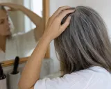 Donna con capelli grigi si tocca la testa, preoccupata che non pettinare i capelli li fa cadere.