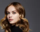 Porträt einer jungen Frau mit welligem, braunem Haar, das mit Balayage-Technik aufgehellt wurde.