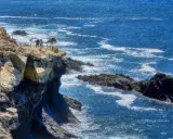 Acantilados rocosos y el mar azul cerca de las cuevas de Ajuy. Turistas observan el paisaje desde un mirador.