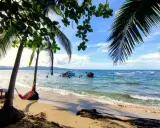 Sonniger Strand in Puerto Viejo mit Palmen, Hängematte und Menschen im türkisfarbenen Meer.