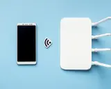 Biały router wifi z antenkami i smartfonem obok. Ikona sygnału wifi symbolizuje połączenie.