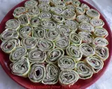 Une assiette rouge remplie de délicieuses crêpes roulées apéritif, garnies de jambon, fromage frais et herbes. Parfait pour un apéritif convivial.
