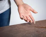 Mano con polvo en los dedos sobre una mesa de madera, mostrando porque sale tanta pelusa en casa.