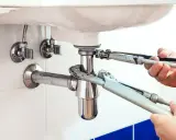 Mains de plombier resserrant un siphon qui fuit sous un lavabo blanc.