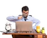 Mężczyzna z lupą bada laptopa, szukając odpowiedzi, czy skstore jest legit. Na biurku budzik, jabłko i sok.