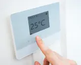 Dedo ajustando uno de los tipos de termostatos para calefacción, mostrando 25°C.