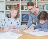 Lehrerin hilft zwei Schülern bei der Nachhilfe Realschule. Sie schreiben konzentriert in ihre Hefte.