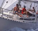 Un groupe profite d'une journée en mer sur ce qui semble être le meilleur voilier fifty, naviguant sur des eaux bleues avec des voiles blanches gonflées par le vent.
