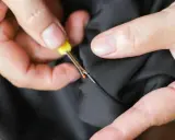 Hands use a seam ripper to open a pocket on black fabric. This is how suit pockets are sewn shut to maintain their shape during shipping.