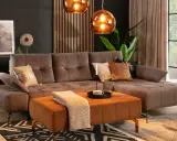 Elegancki salon z sofą w kolorze taupe. Idealnie komponuje się z pomarańczowym pufem, miedzianymi lampami i złotymi dodatkami.