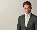 A man in a dark green suit and white shirt with a cream tie. This timeless look embodies the perennial suit meaning of enduring style and sophistication.
