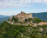 Borgo medievale su una collina verde, uno dei tanti **paesi da vedere vicino Roma**, con case in pietra e un campanile.