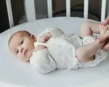 Noworodek w białej koszulce leży w łóżeczku, a ręce dotykają jego stóp.