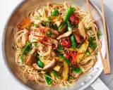 Pyszny makaron sojowy z kurczakiem, warzywami i papryczką chili, podany w metalowej patelni z pałeczkami.