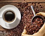 Eine Tasse heißer Kaffee neben einer Schaufel voller gerösteter Bohnen und einem Jutesack. Der Duft von perfekt gebrühtem Filterkaffee liegt in der Luft.