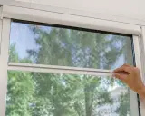 Main tenant ajuste sa moustiquaire de fenêtre pour profiter de l'air frais sans insectes.