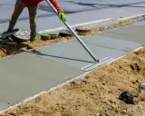 Robotnik wygładza świeży beton na chodniku za pomocą kielni.