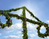 En midsommarstång, klädd i grönska och blommor, reser sig mot en klarblå himmel med solsken.