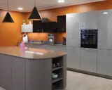 Cuisine moderne avec îlot central et armoires grises. Les murs orange vif contrastent avec les surfaces épurées, créant une ambiance chaleureuse. Une cuisine sans hotte, mais avec un design élégant.