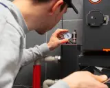 Technik sprawdza manometr kotła gazowego, by dowiedzieć się, jak najlepiej ustawić ogrzewanie gazowe. W ręku trzyma smartfon.