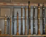 Une collection d'instruments à vent anciens, une véritable famille des vents, alignés sur un mur boisé.