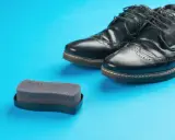 Czarne buty ze sztucznej skóry i gąbka do pastowania. Czy można pastować buty ze sztucznej skóry? Tak, specjalnymi preparatami.