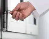 Dłoń z kluczem imbusowym reguluje zawias drzwi balkonowych. Dowiedz się, jak naprawić drzwi balkonowe.
