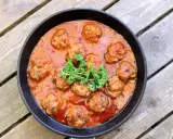 Frikadeller i tomatsås, en klassisk svensk rätt, serveras i en gjutjärnspanna. Garnerad med persilja.