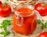 Un bocal de sauce tomate maison, avec des tomates fraîches et du basilic disposés autour.