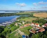 Malowniczy widok na jezioro z przystanią pełną żaglówek, idealne miejsce na długi weekend czerwcowy. W oddali pola i zabudowania.