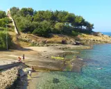 Scogliera e mare cristallino a San Gregorio Leuca. Persone si godono il sole e l'acqua, una scalinata sale verso la collina alberata.