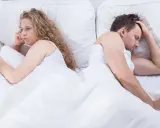Para, odwróceni do siebie plecami w łóżku, zmartwiona kobieta i mężczyzna z ręką na czole. Czy to pochwica? Co to za problem?