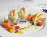 Recette entrée froide gastronomique facile : crevettes et avocat en verrine, saumon fumé roulé, toasts grillés, tomates cerises et fleurs comestibles.