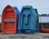 Plusieurs petites embarcations colorées, dont une annexe orange, sont rangées sur le quai, face à la mer.