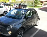 Frau lehnt sich aus einem grauen Fiat 500 Cabrio, bereit für eine Spritztour. Hier sind einige mietwagen portugal tipps für Ihren Urlaub!