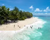 Spiaggia tropicale con palme e persone che nuotano nell'acqua cristallina dell'atollo di Maafushi.