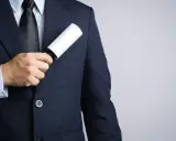A man in a dark tuxedo uses a lint roller to clean his jacket, showing a simple way how to clean a tuxedo.