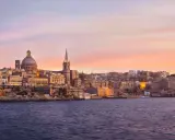 Valletta, Malta, im Dezember bei Sonnenuntergang. Das malerische Malta Wetter im Dezember zeigt sich hier von seiner schönsten Seite, mit warmen Farben am Himmel über der historischen Stadt.