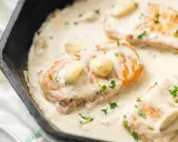 Aromatyczny kurczak w sosie śmietanowo-czosnkowym, podany w żeliwnej patelni, posypany świeżą natką pietruszki.