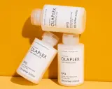 Drei Flaschen der OLAPLEX Serie, "Hair Perfector No.3", liegen übereinander auf einem orangen Hintergrund.