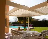 Une pergola bioclimatique moderne avec des lames orientables protège un salon extérieur et une piscine.
