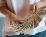 Dłonie trzymają wachlarz polskich banknotów. Zastanawiasz się, czy nagroda jubileuszowa wlicza się do emerytury?