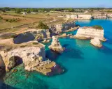 Scogliere bianche e mare turchese in una splendida **Puglia estate**. Faraglioni emergono dall'acqua cristallina, un vero paradiso.