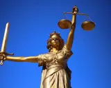 Statua dorata della Giustizia con spada e bilancia, simbolo dei giudici ordinari, contro un cielo blu intenso.