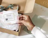 Tarjeta de agradecimiento tamaño postal con código QR, dentro de una caja de regalo abierta con papel de seda dorado.