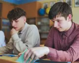 Uczniowie w klasie, jeden z nich zamyślony, inny przegląda notatki. Czyżby czekał na ocenę, która może oznaczać nieklasyfikowanie ucznia?