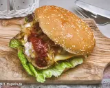 Ein saftiger vegetarischer Burger mit Salat, karamellisierten Zwiebeln und scharfer Sauce auf einem Holzbrett.